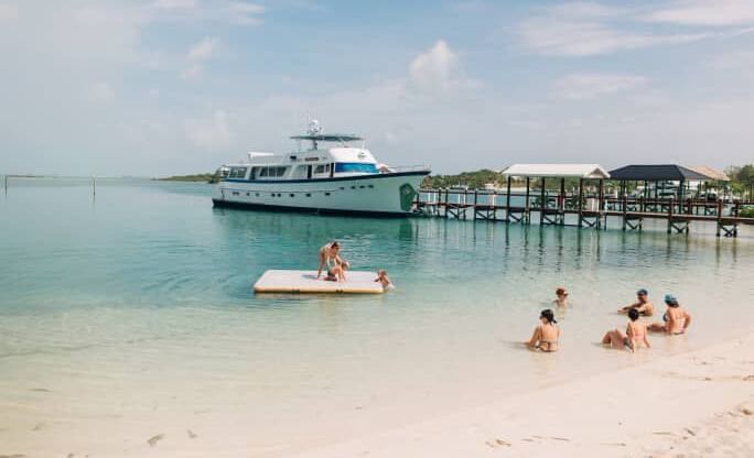 Shoreline with dock, anchored boat, people in swimwear in shallow water, Abaco Inn.