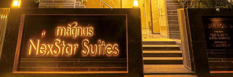 Magnus Nextar Suites facade with yellow highlighted text and a glimpse of the entrance, shot during the late evening.