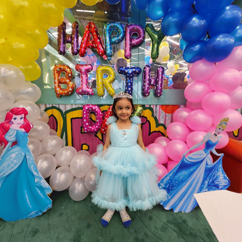 A child in a princess dress standing in front of a vibrant birthday backdrop at Central Courtyard Hotel.