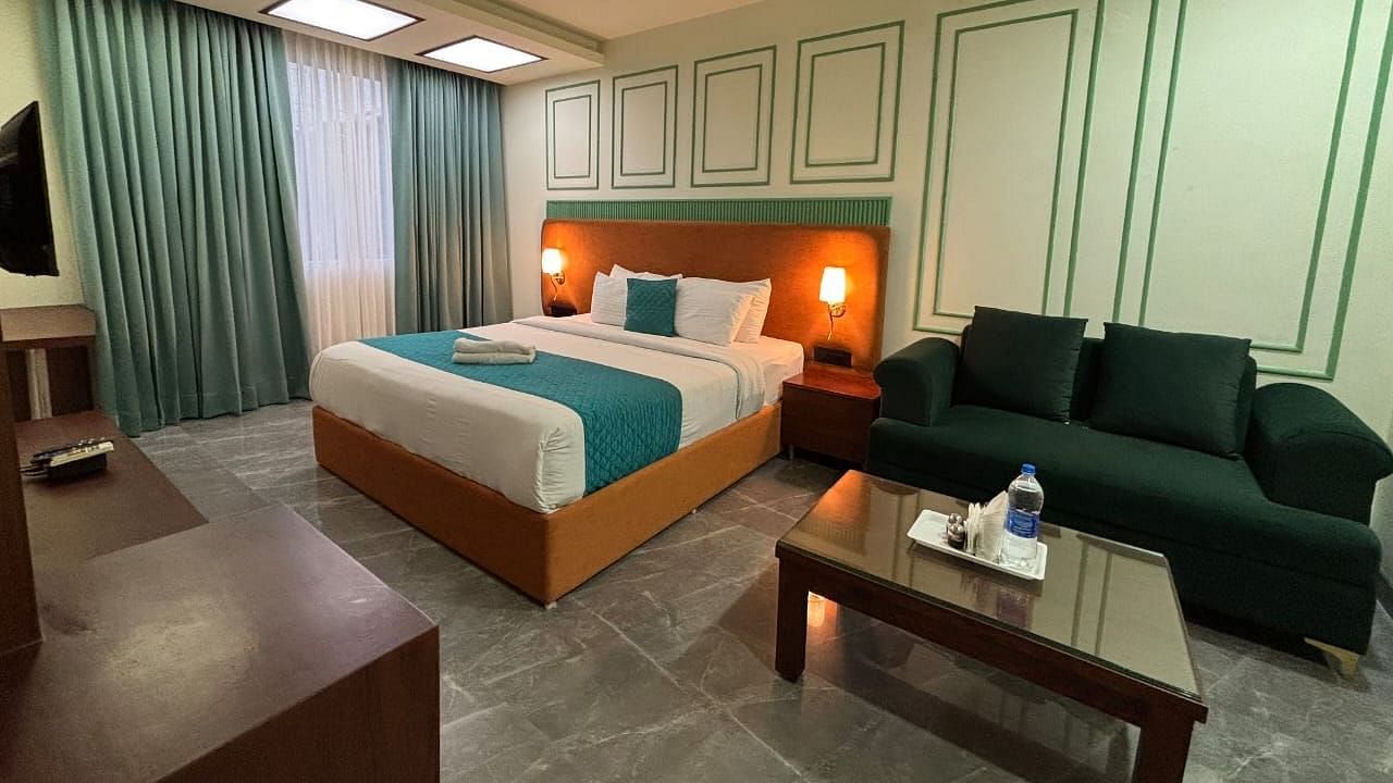 A spacious room with a double bed, a dark green sofa, and a wooden coffee table - Asian Suites IFFCO Metro, Gurgaon