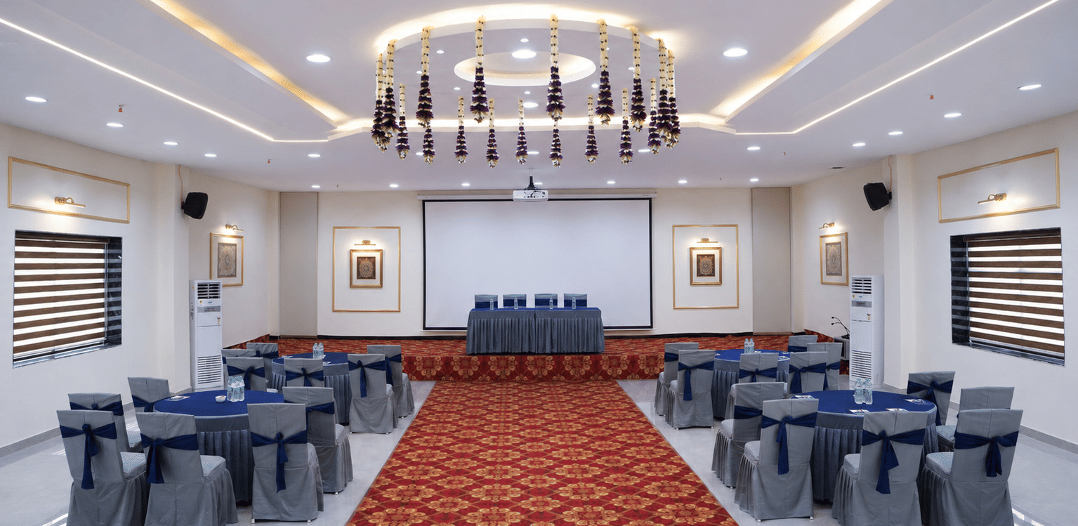 The large banquet hall setup of Galadari Boardroom at Hotel Galadari with round dining tables, chairs, a main stage, and overhead floral decorations.