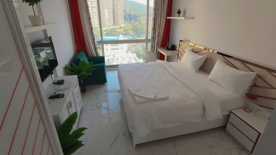 deluxe room at Maxxvalue Hotel, Chitranjan Tower, Powai with a posh bed and white linens along with floor-to-ceiling windows offering ciy view1