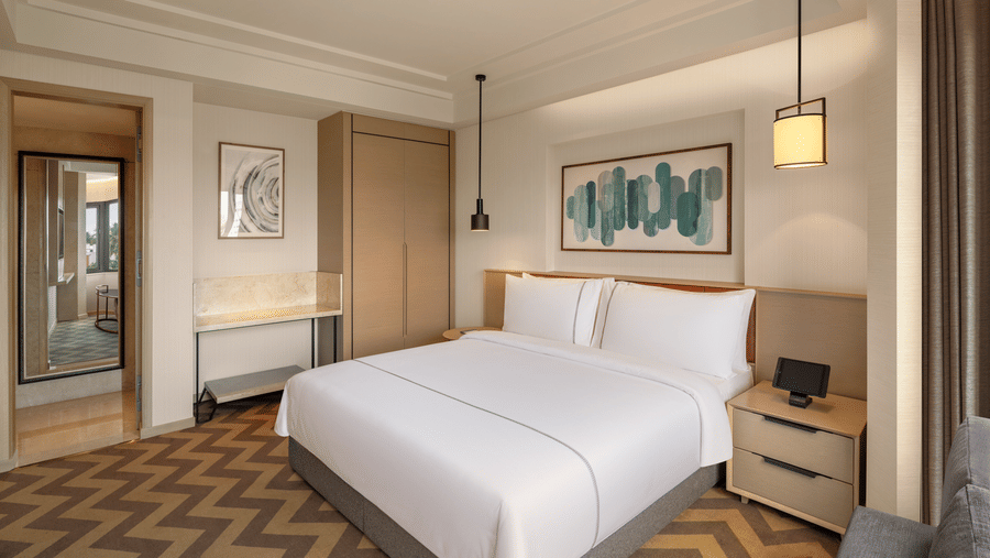 Suite room at The Residency Chennai, featuring a king-sized bed, stylish hanging bedside lights, and a corner wall mirror.