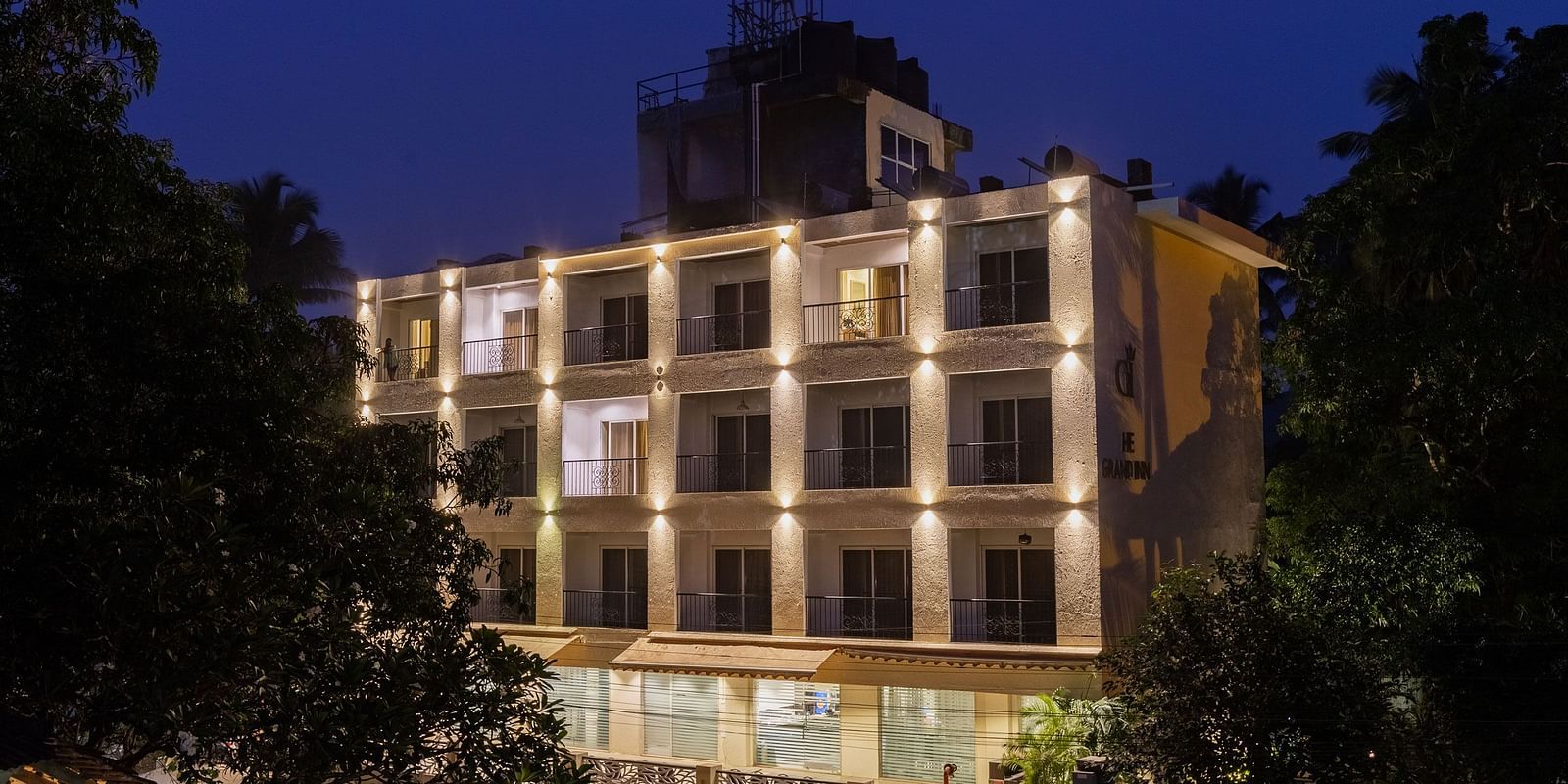 Facade of Calux Grand Inn, Calangute with trees on the sides with a clear sky in the background.