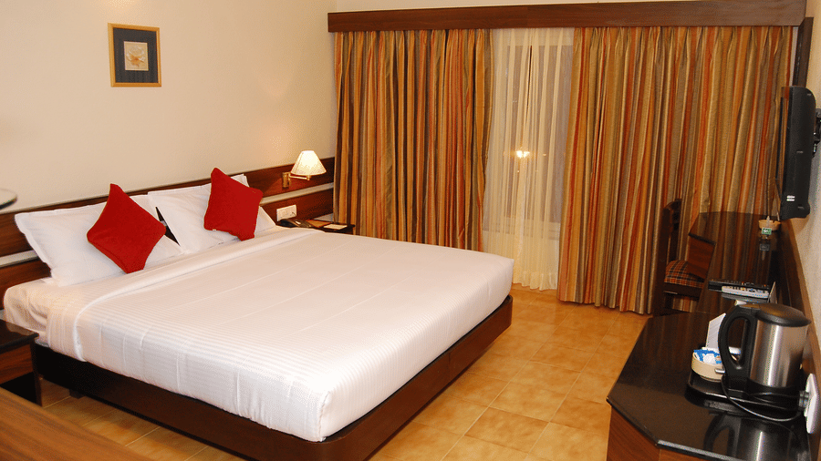 The spacious Deluxe bedroom at Green Pastures, Kodai, showcasing a magnificent large bed with crisp linens, accented by decorative pillows, and complete with a convenient hot beverage station near the window.