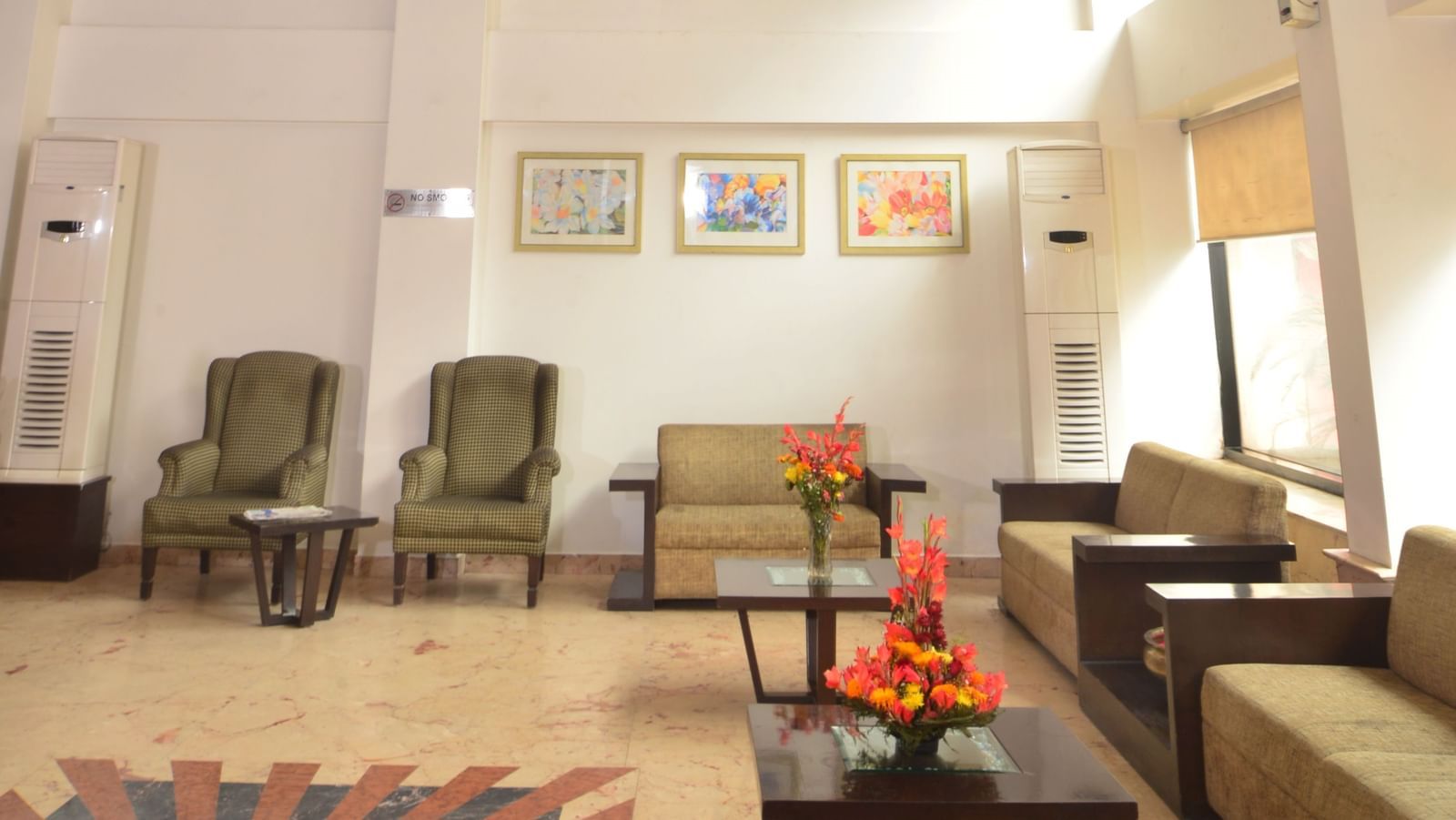 Lobby of Le ROI Delhi Hotel Paharganj featuring a seating area with chairs, sofas, and centre tables where flowers are placed.