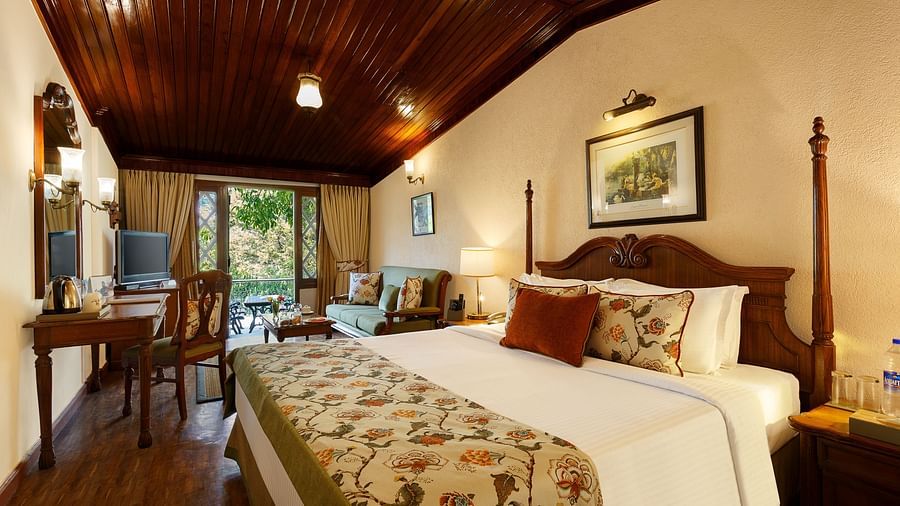 A full view of a room with bed, chair, table and a huge glass window with sloped roof - the naini retreat, nainital.
