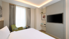 A bright hotel room at Riviera Sarovar Portico, Pathankot, with a large bed, a wall-mounted television, and modern decor.