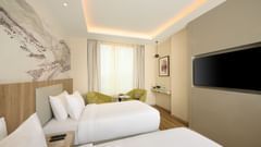 A bright hotel room at Riviera Sarovar Portico, Pathankot, with twin beds, a wall-mounted television, and modern decor.