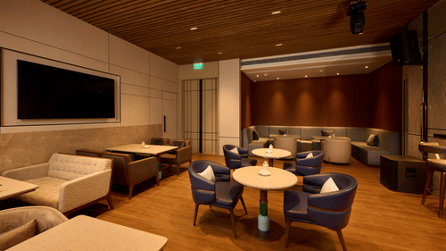 The restaurant lounge area with tables, chairs, and a large screen television at Riviera Sarovar Portico, Pathankot.