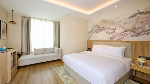 Room with double bed, wall art, window seating and natural light at Riviera Sarovar Portico, Pathankot.