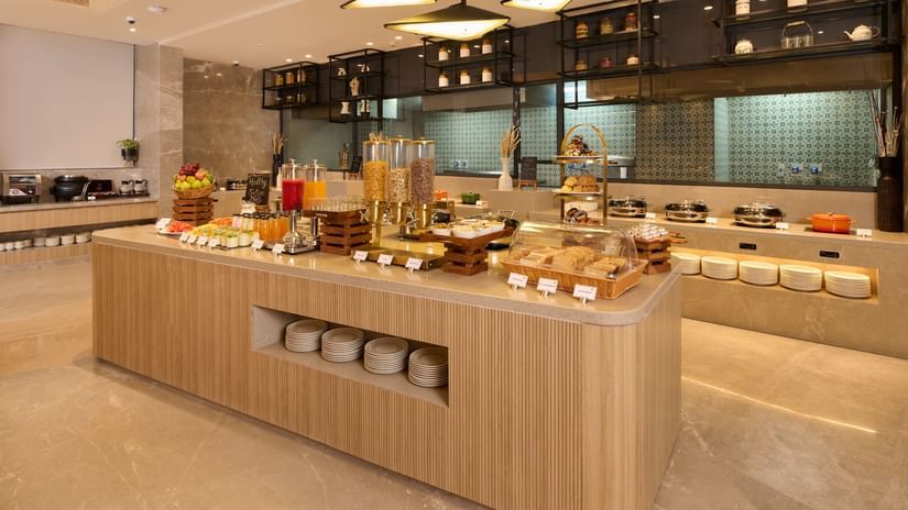 The hotel's breakfast buffet with food and drinks on a central counter at Riviera Sarovar Portico, Pathankot.