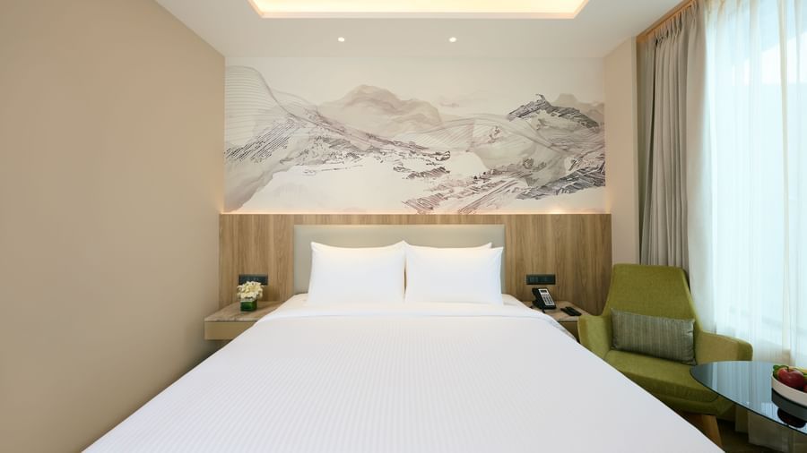 A comfortable and inviting hotel room at Riviera Sarovar Portico, Pathankot, featuring a large, neatly made bed and a soft chair.