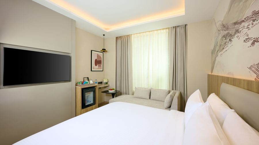 A bright hotel room at Riviera Sarovar Portico, Pathankot, with a large bed, a wall-mounted television, and modern decor.
