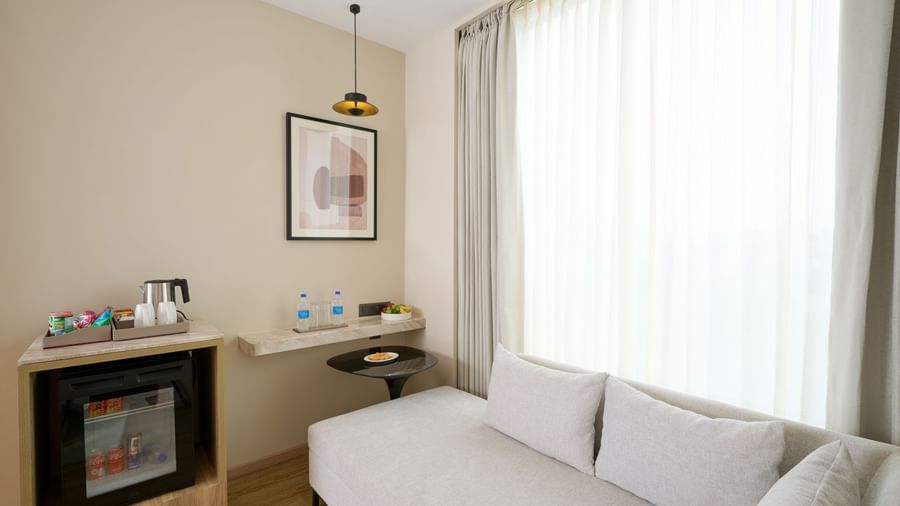 Room corner with sofa, minibar, tea and coffee setup by a large window at Riviera Sarovar Portico, Pathankot.