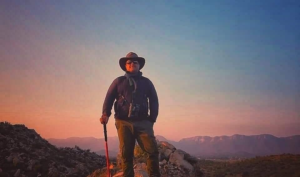 An image of a person standing on a hilltop with a dusky sky as the backdrop