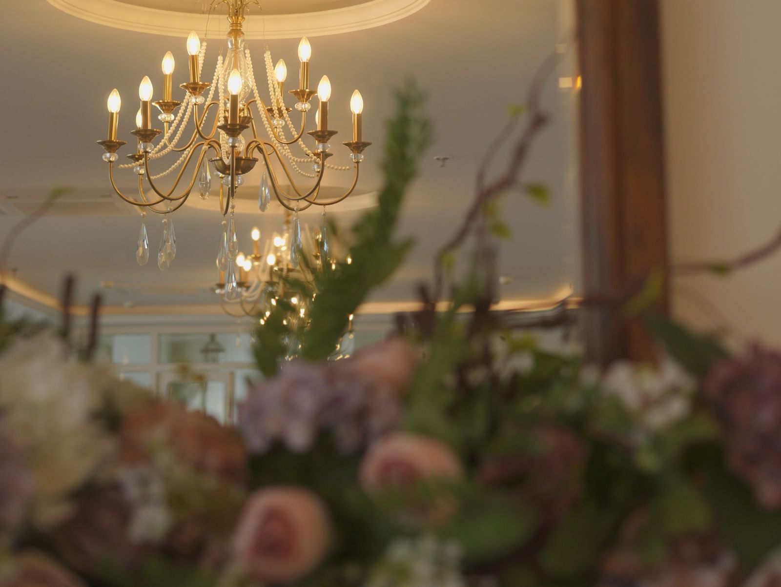 Floral arrangement in front of a large mirror reflecting a chandelier - Mayfair Cafe & Suites, Dalhousie