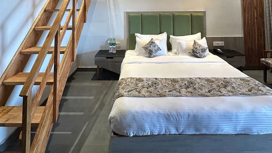 A spacious hotel room with a king size bed, a wooden ceiling, and a loft area accessible by a staircase.