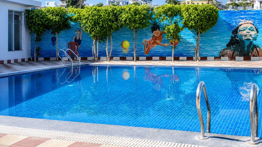 Outdoor swimming pool bordered by trees with a colourful painted mural on the wall at Eastlynn Resort, Rishikesh.