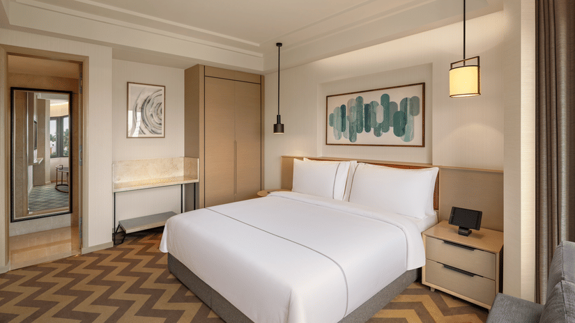 Suite room at The Residency Chennai, featuring a king-sized bed, stylish hanging bedside lights, and a corner wall mirror.