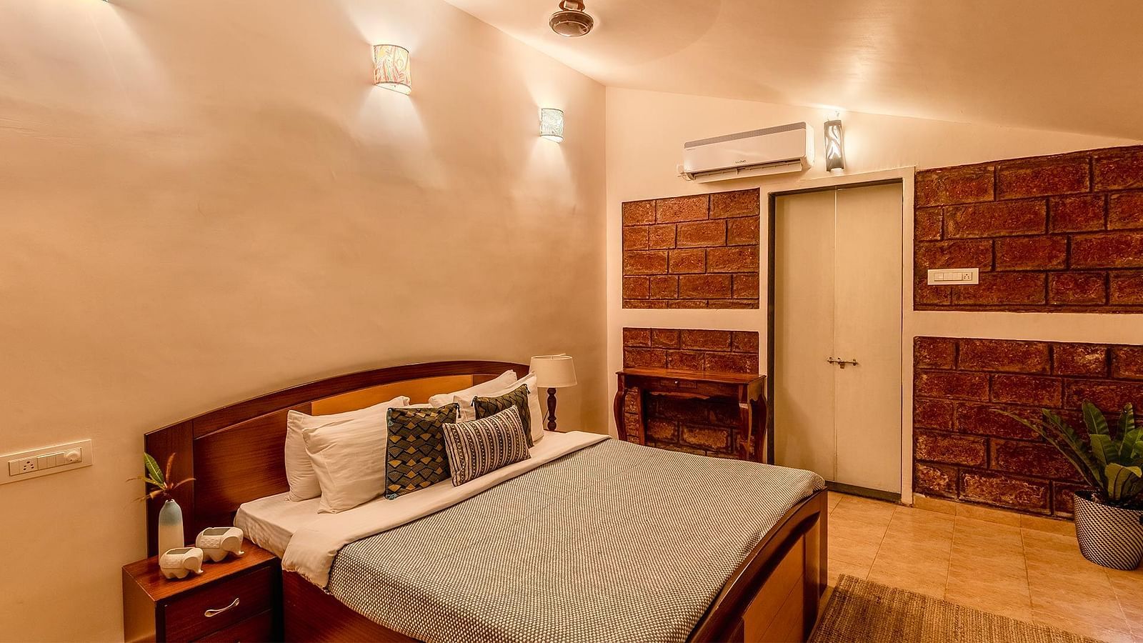 A double bed room with a side table with amenities, lights, ceiling fan, wooden floor and door