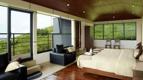 A side angle view of the suite at the villa featuring a king size bed with two sofas and a private balcony overlooking the mountains Shot of the facade of the villa with an artificial pond in front of it | Ibex Stays and Trails, Valparai (Tale Rock)