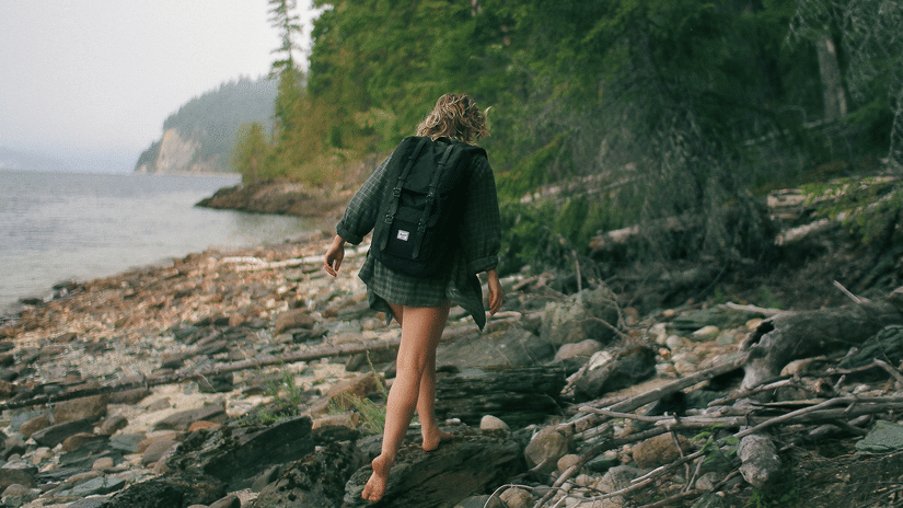 A woman walking on a rocky seashore.