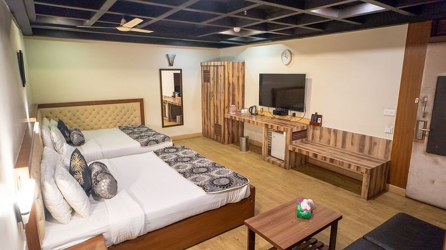 Family Room featuring two beds, a wooden bench, a small table, and a television.- Hotel Ashok Nagpur