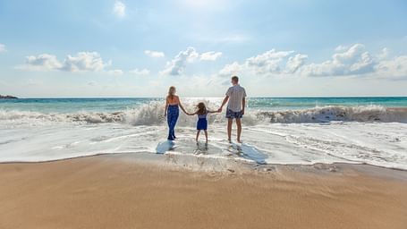 a family of 3 holding hands on a beach