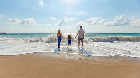 A family holding hands and walking into the waves, enjoying a sunny day at the beach together.