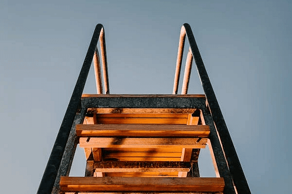  A wooden staircase leads upwards against a plain, light-colored background.