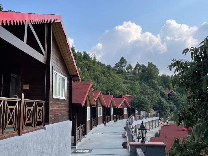 A scenic pathway winding between charming cottages with distinctive red roofs, showcasing the resort's picturesque setting - Digantaa Resort in Mukteshwar.