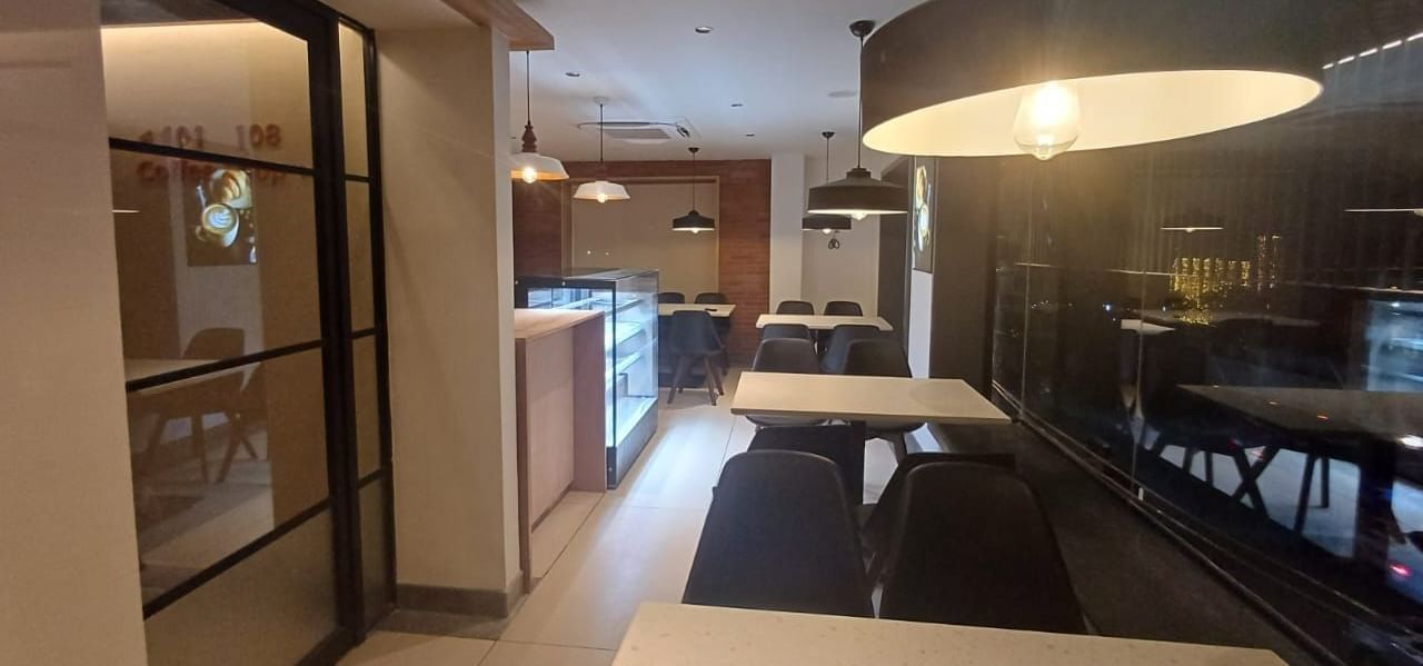 The Brew House at Hotel Raai, Hosur featuring seating arrangement with chairs and table in L shape. On each table there is a light bulb hanging from top.