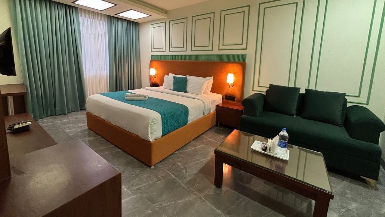 A spacious room with a double bed, a dark green sofa, and a wooden coffee table - Asian Suites IFFCO Metro, Gurgaon