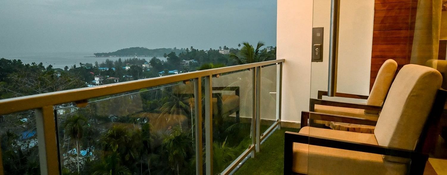 A hotel balcony with a glass railing and comfortable outdoor chairs, providing a sweeping view of the coastal landscape and the sea - Sea Hills Hotels, Sri Vijaya Puram (Port Blair)