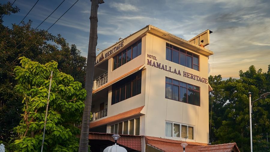 The exterior of Hotel Mamallaa Heritage from a slightly different angle, showcasing its multi-story structure and architectural details under a pleasant sky.