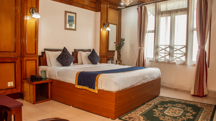 An image of a Hill Club room featuring a double size bed, a bedside table, jug, tea and coffee maker on the other table, and a mirror at Central Hill Resort, Gangtok