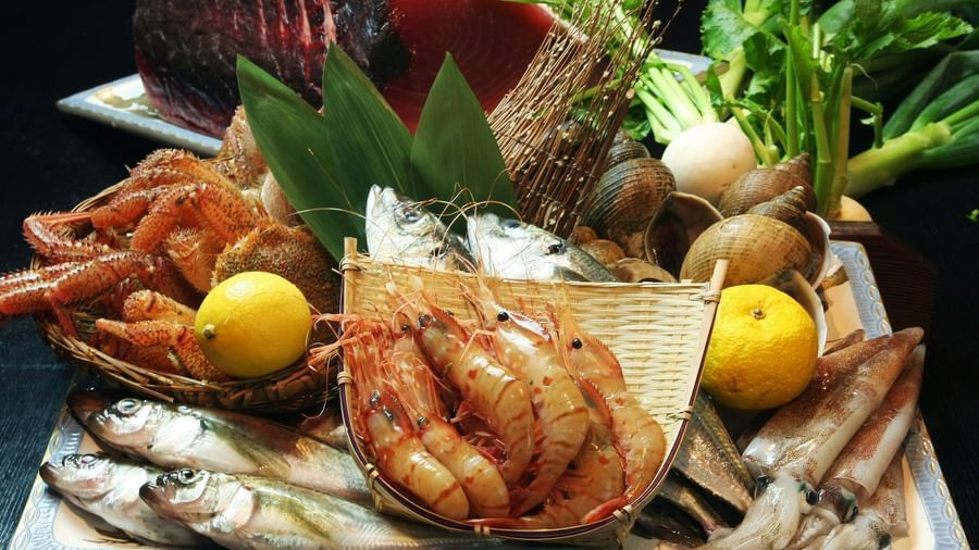 An assortment of cooked seafood, including fish, scallops, and shrimp, arranged on a large platter with lemons and leafy greens.