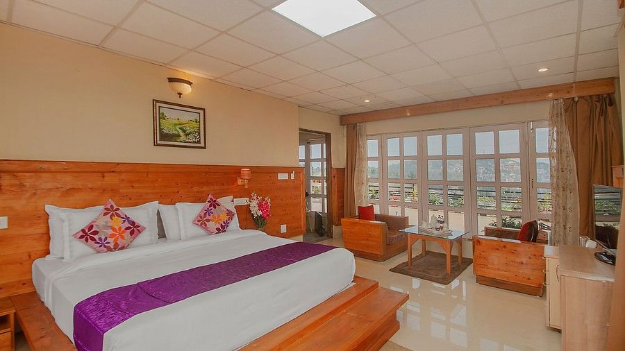 A spacious hotel room with a wood-panelled bed, purple accents, large windows, and a sitting area with a scenic outdoor view - Mount Hotels