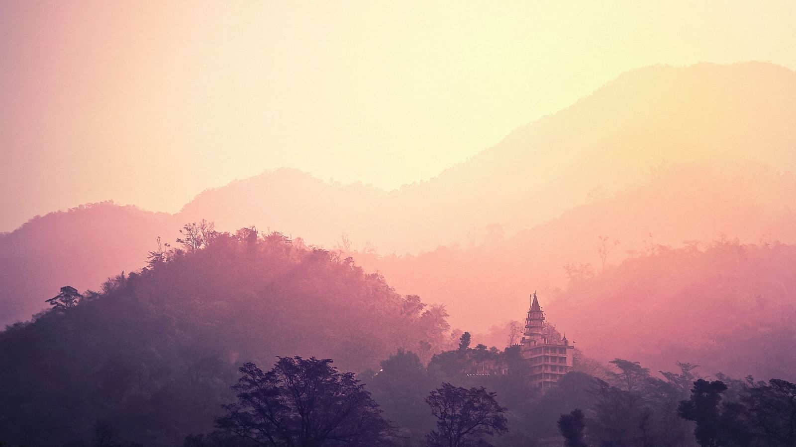 The yellow and orange sky overlooks a temple and surrounding hills.