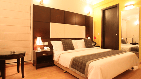 A sophisticated boutique hotel bedroom with a large bed, dark wood furniture, and soft, warm lighting for a relaxing and cosy atmosphere at Emblem Hotel, New Friends Colony, New Delhi.