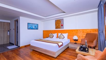 Elegant bedroom at Sumitel Premier Inn, Siliguri, featuring a cosy bed, soft lighting, wooden interiors, and seating chairs creating a warm and welcoming stay.