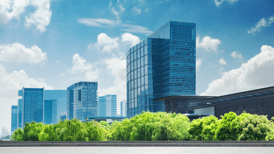 Glass office buildings surrounded by green trees under a blue sky