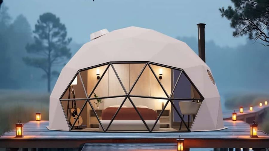 Exterior view of a Glass Dome room at dusk, with ambient lighting and a wooden deck surrounded by trees.