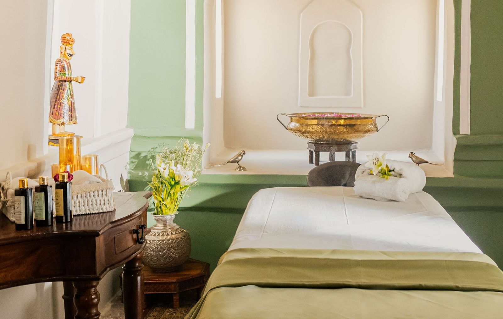 A serene spa treatment room with soft lighting, featuring a massage table, arched alcove, and calming green accents.