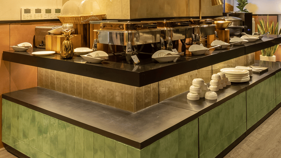 A buffet serving station inside Koi Garden. Covered dishes rest on the counter surface under lighting. The restaurant logo is fixed to the pillar structure above.
