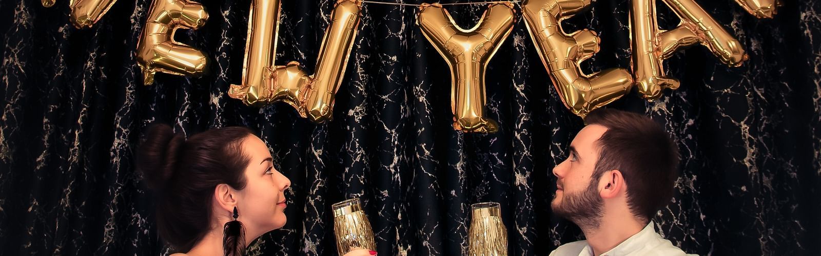 a couple holding a glass of champagne and looking at Happy New Year made out of ballons