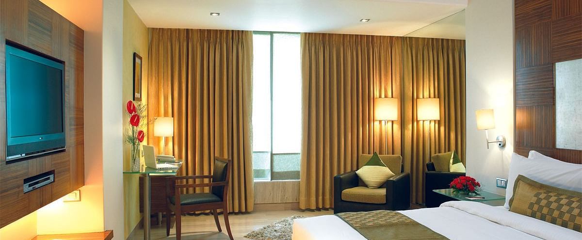Image of a the executive room featuring a king size bed, a study table and chair, flat screen television, and an expansive window with golden curtains. | Mirage Hotel