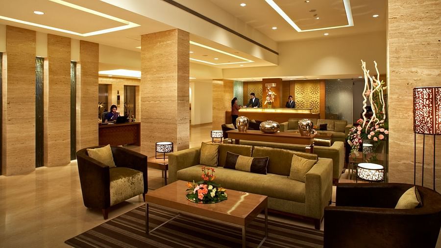An image of a reception lobby featuring sofa sets, centre table, reception desks, and a few people standing at Adarsh Hamilton