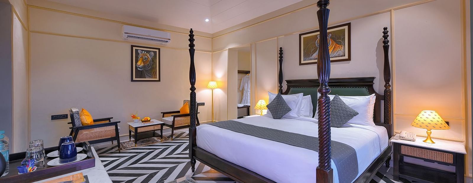Luxury Suite Cottage with a dark wood four-poster bed, a seating area with orange-cushioned chairs, patterned flooring, and framed artwork - Singhvilas, Ranthambore
